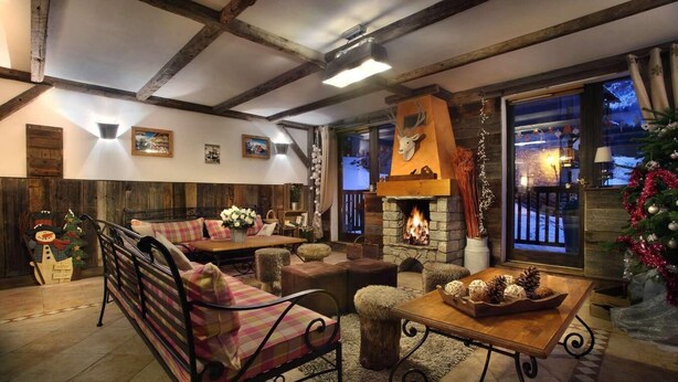 A cozy living room with a fireplace, wooden beams, and a large window overlooking a snowy landscape.