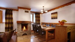 A cozy dining area with a stone fireplace, wooden furniture, and a chandelier.