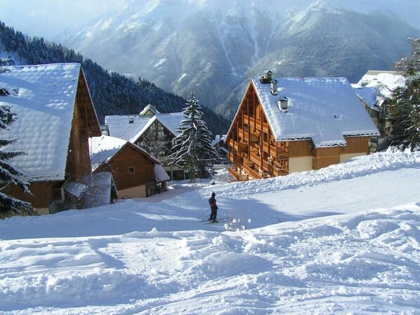 A snow-covered village with wooden houses and a person skiing. - 50m from ski slopes, fitness, swimming pool, sauna, hammam, balcony, tv, ski locker, 32m², Oz 3300 (Oz)