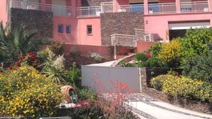 Un edificio a due piani con facciata rosa, dettagli in pietra e un giardino curato con diverse piante e fiori.