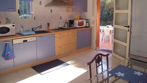 Una cucina compatta con forno a microonde, piano cottura e lavello. Si intravede un'area pranzo con tavolo e sedie attraverso una porta aperta.