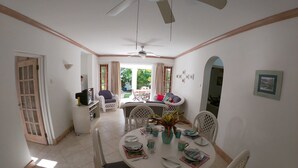 Un coin repas avec une table ronde, des chaises blanches et un ventilateur de plafond.