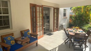 Une terrasse ensoleillée avec un canapé et une table en bois, un coin repas avec des chaises et une vue sur le jardin.