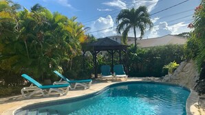 Une piscine entourée de chaises longues, de végétation tropicale et d’un belvédère.