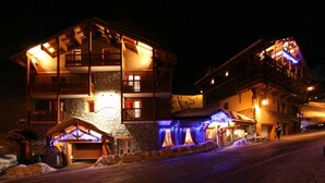 A multi-story building with balconies and a stone facade, featuring a ski lift and illuminated decorations. - 50m from ski slopes, fitness, swimming pool, sauna, balcony, fireplace or stove, tv, ski locker (Val Thorens)