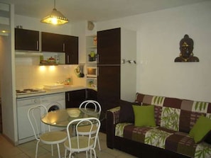 Um espaço compacto com cozinha compacta, mesa de jantar com cadeiras e sofá com almofadas.