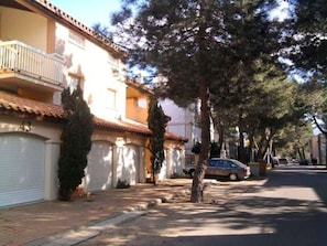Rua residencial com casas, árvores e um carro estacionado.