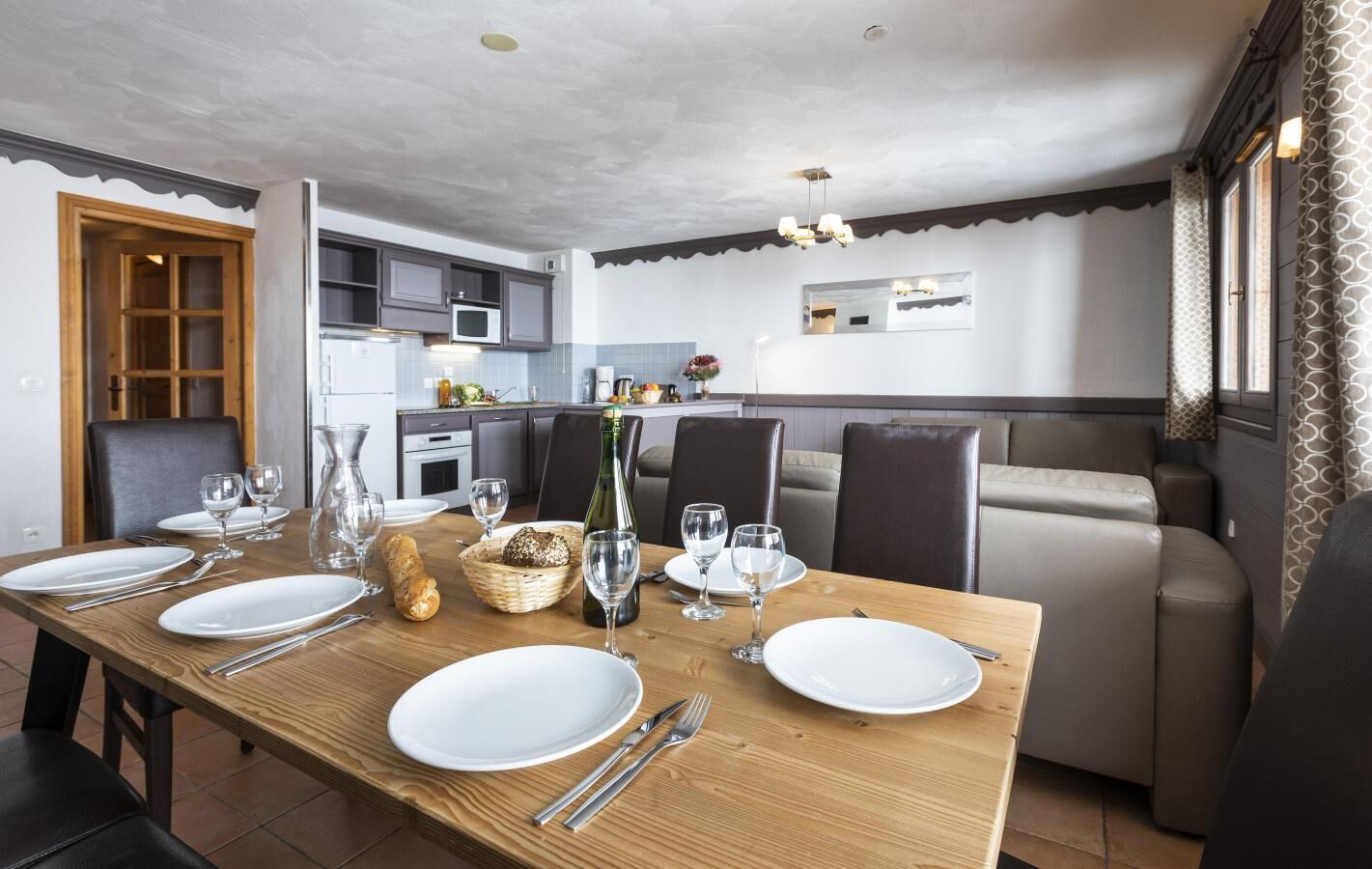 A dining area with a wooden table set for four, a kitchen in the background, and a seating area with a sofa and chairs.