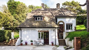 A two-story house with a white exterior, a small front porch with a table and chairs, and a brick chimney. - A lovely, modern apartment just 350 yards from the beach. (St Margaret&rsquo;s Bay)