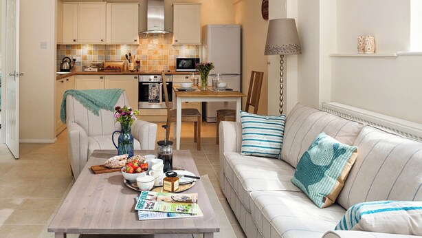 A modern kitchen with a dining area, a sofa with striped pillows, and a coffee table with breakfast items. - A lovely, modern apartment just 350 yards from the beach. (St Margaret&rsquo;s Bay)
