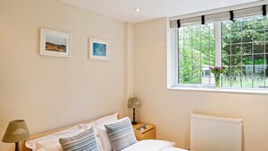 A neatly made bed with striped pillows, a bedside lamp, and a window with a view of greenery. - A lovely, modern apartment just 350 yards from the beach. (St Margaret&rsquo;s Bay)