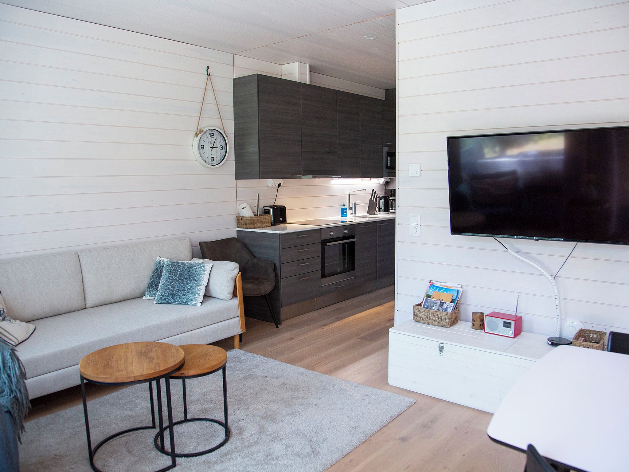A modern living room with a sofa, two coffee tables, a TV, and a kitchen area with cabinets and appliances.