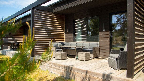 Un área de estar exterior moderna con terraza de madera, asientos integrados y grandes ventanales.