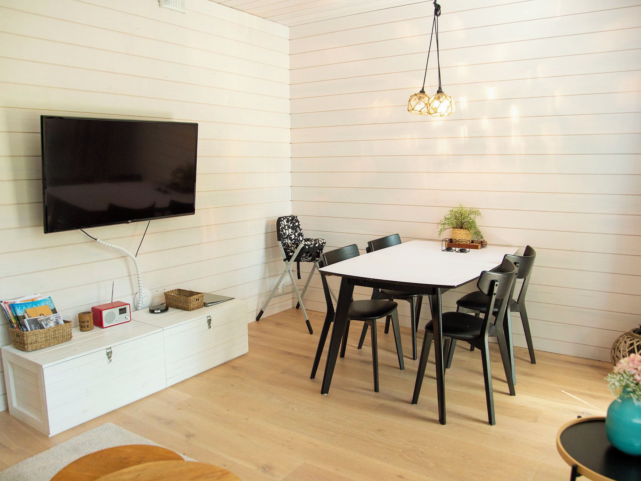 Uma sala de estar moderna com televisão de tela plana, uma mesa de jantar com cadeiras, um armário branco e um pequeno rádio.