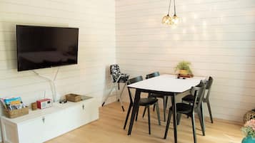 Uma sala de estar moderna com televisão de tela plana, uma mesa de jantar com cadeiras, um armário branco e um pequeno rádio.