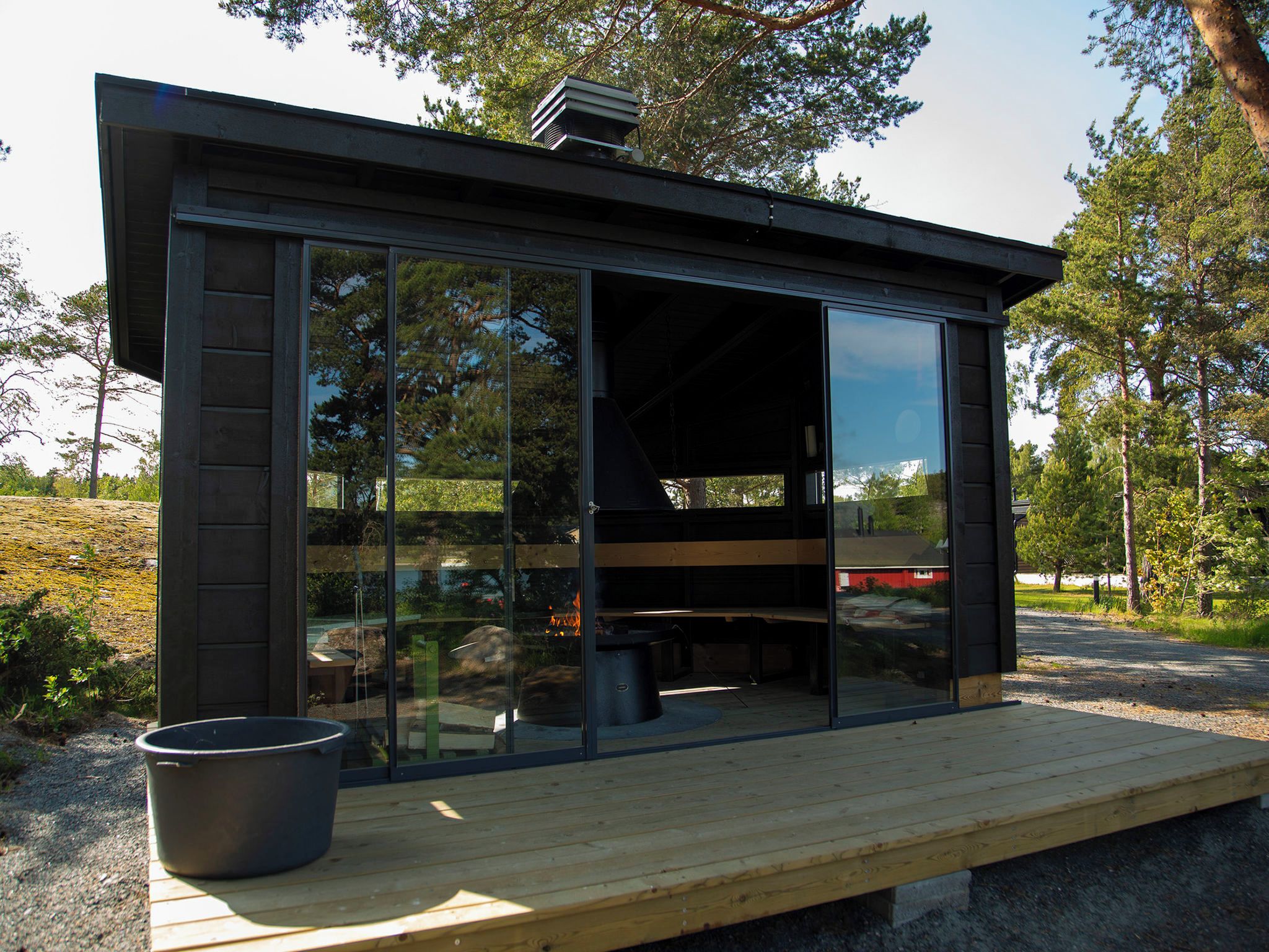 A modern outdoor structure with a glass enclosure, a wooden deck, and a fire pit.