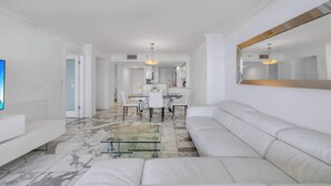 Una sala de estar moderna con un sofá blanco, una mesa de centro de vidrio y una zona de comedor con una mesa y sillas blancas.