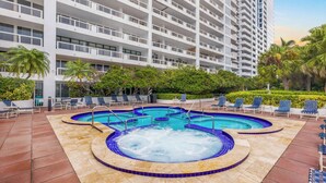 Un hotel con piscina en la azotea, que incluye un jacuzzi, sillones de descanso y vistas a un edificio alto.