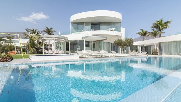 Un hotel moderno con una piscina grande, sillas de descanso y una edificación circular peculiar.
