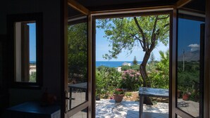 Puerta abierta que da a un patio con vista al mar, un árbol y plantas en macetas.