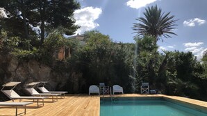 Una terraza de madera con piscina, sillas de descanso y un acantilado rocoso al fondo.