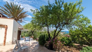 Un patio con mesa y sillas blancas, una palmera y vista al mar.