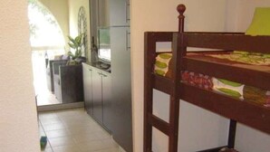 Una habitación pequeña y funcional con una cama tipo litera, kitchenette y vista al exterior.