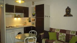 Un espacio habitable compacto con kitchenette, una mesa de comedor con sillas y un sofá con cojines.