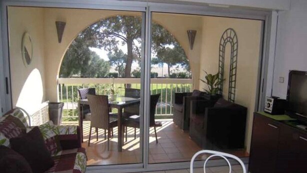Una habitación con puerta corrediza de vidrio que da a un patio exterior, mesa de comedor con sillas, sofá y televisor sobre un mueble.