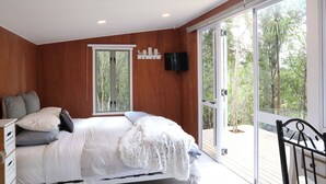 Une chambre à coucher comprenant un lit, une commode, un téléviseur et une porte-fenêtre coulissante donnant sur un balcon.