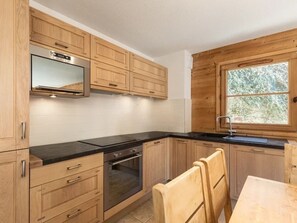 A modern kitchen with wooden cabinets, a built-in oven, a black countertop, and a window with a view of trees.