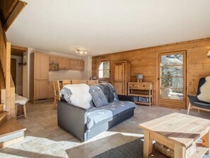 A cozy cabin interior with a sofa, wooden cabinets, a dining table, and a large window.