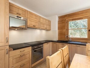 A modern kitchen with wooden cabinets, a built-in oven, a black countertop, and a window with a view of trees.