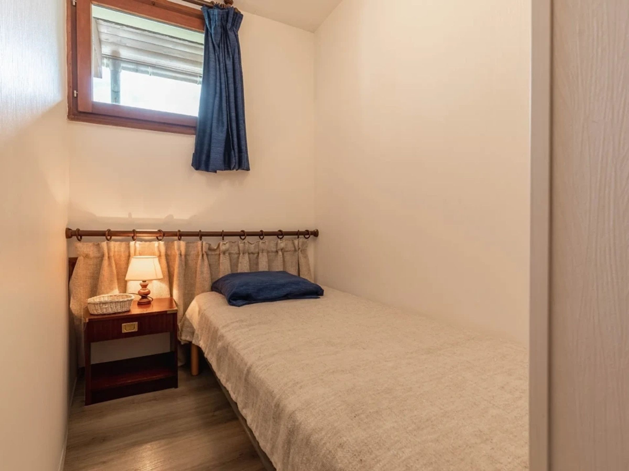A small bedroom with a single bed, a nightstand with a lamp, and a window with curtains.