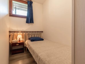 Ein kleines Schlafzimmer mit einem Einzelbett, einem Nachttisch mit Lampe und einem Fenster mit Vorhängen.