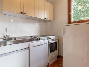 Een keuken met witte kastjes, een roestvrijstalen spoelbak, een kookplaat, een oven en een koelkast.