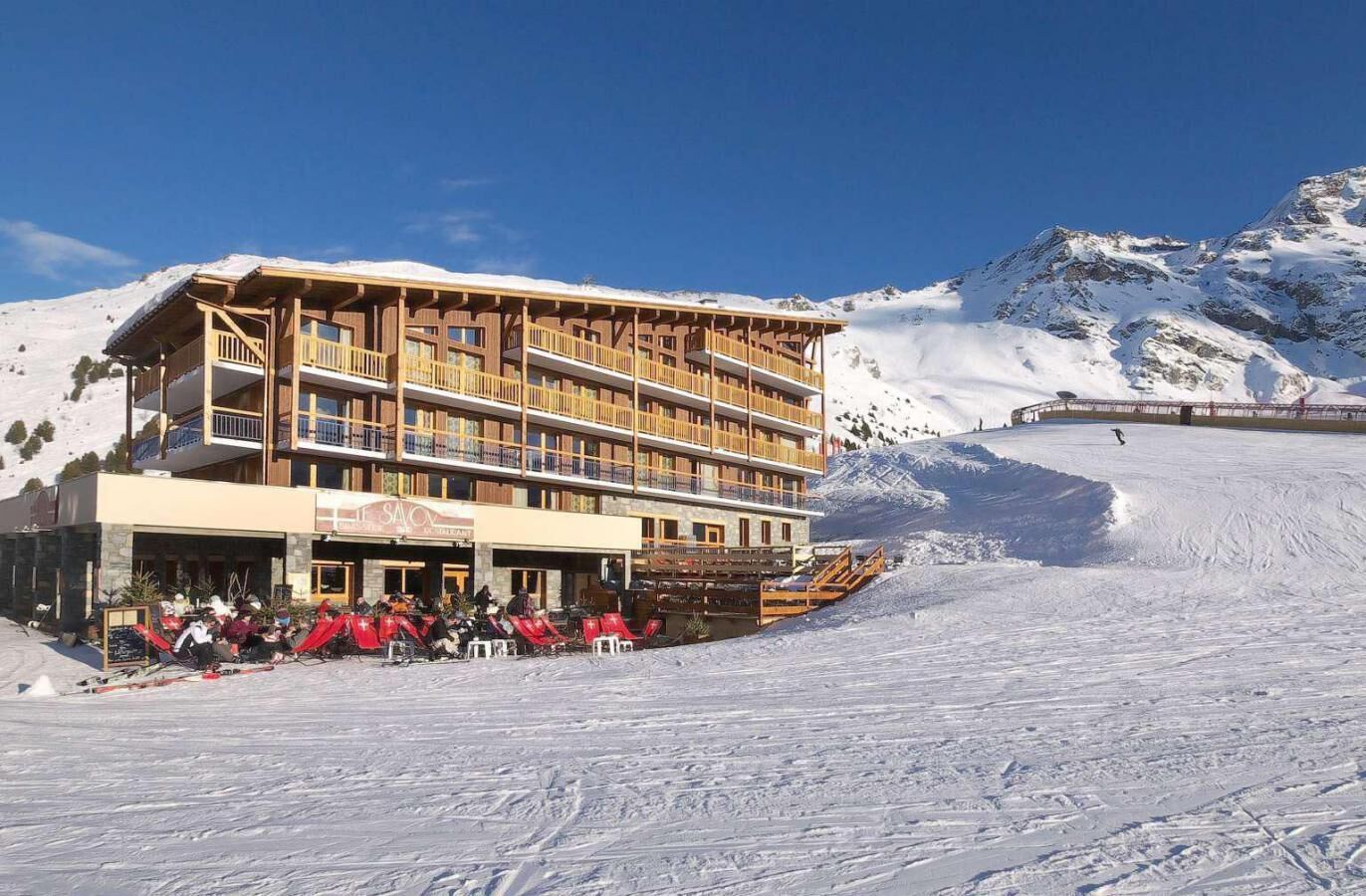 Un hôtel à plusieurs étages doté d’une terrasse, de pistes de ski et, en arrière-plan, de montagnes enneigées.