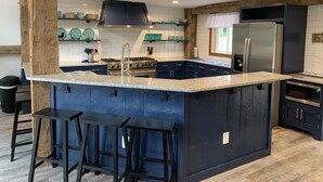 Uma cozinha moderna com armários azul-escuro, bancada de granito, eletrodomésticos de aço inoxidável e uma ilha embutida com banquetas.