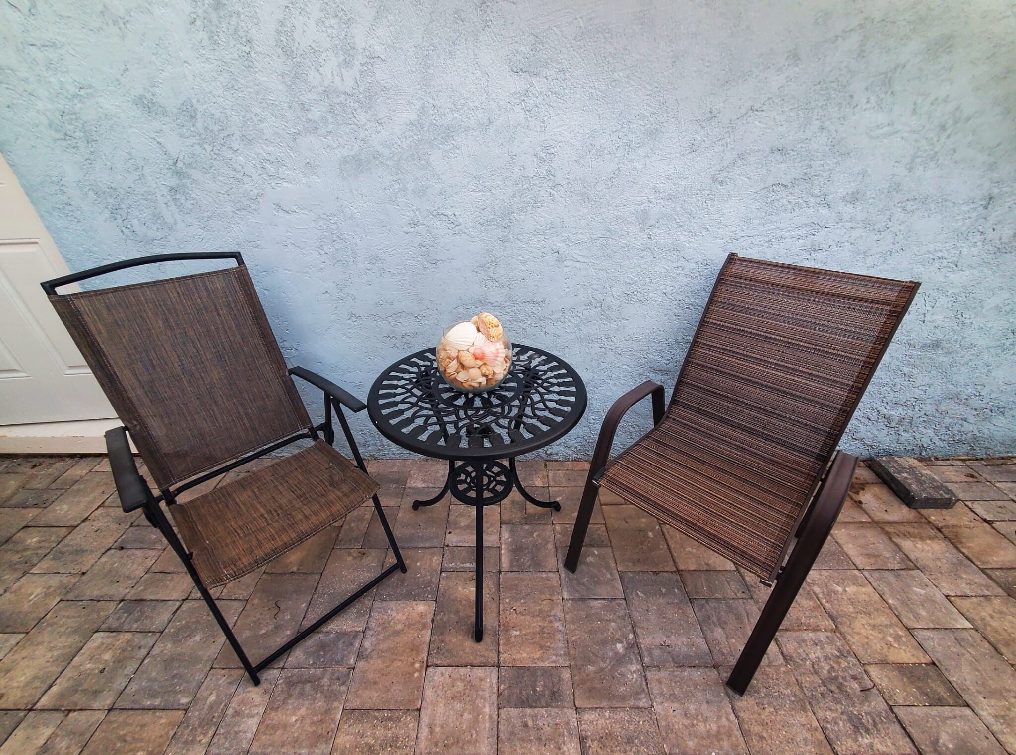 A patio area with two chairs and a table, featuring a blue textured wall and a tiled floor.