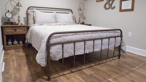 Un dormitorio ordenado con una cama con estructura de metal, una mesita de noche con lámpara y un reloj de pared.