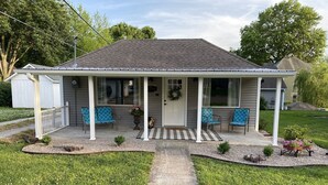 A single-story house with a covered porch, two blue patterned chairs, and a small garden area with a pathway leading to the entrance. - Das Gästehaus • 50 Min to KC Stadium • World Cup 2026 (Concordia)