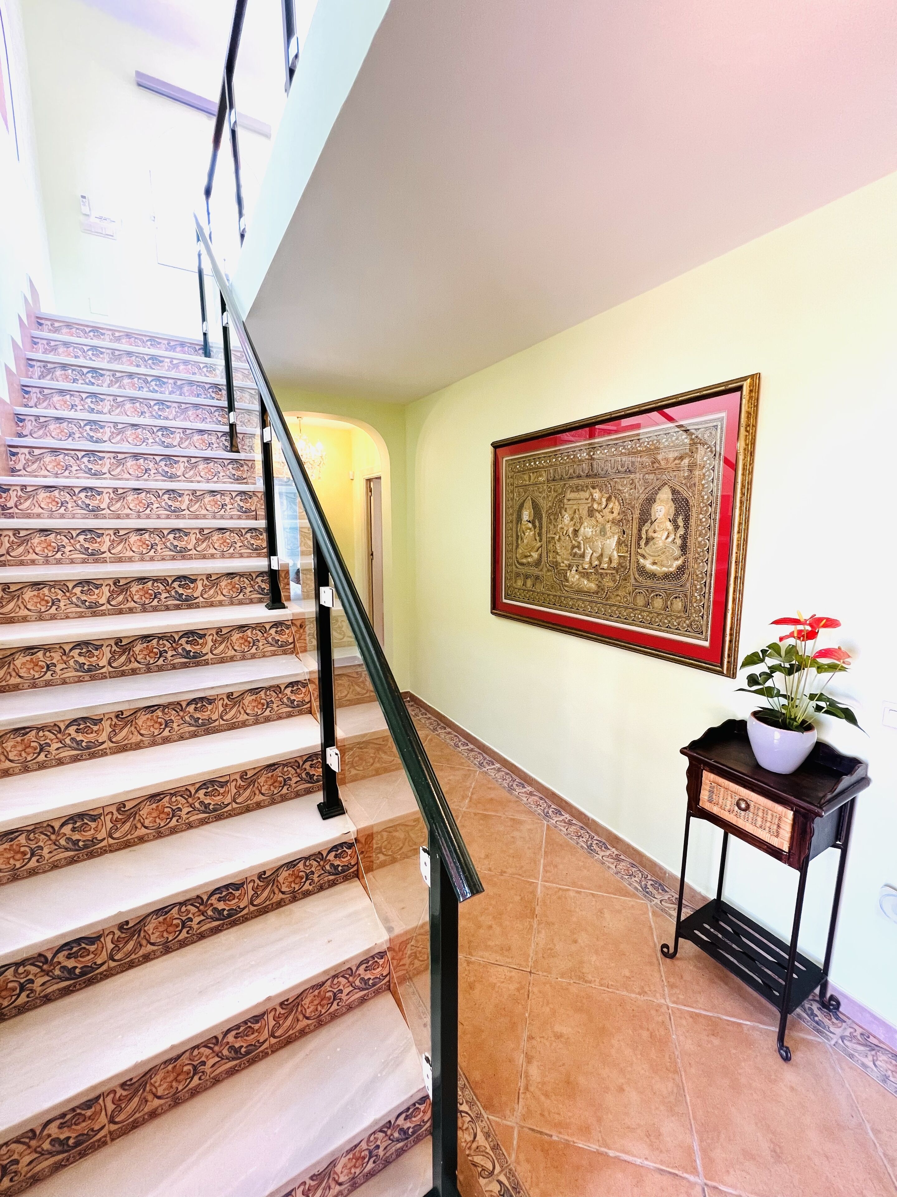 A staircase with ornate railings, a wall-mounted framed artwork, and a small table with a potted plant.