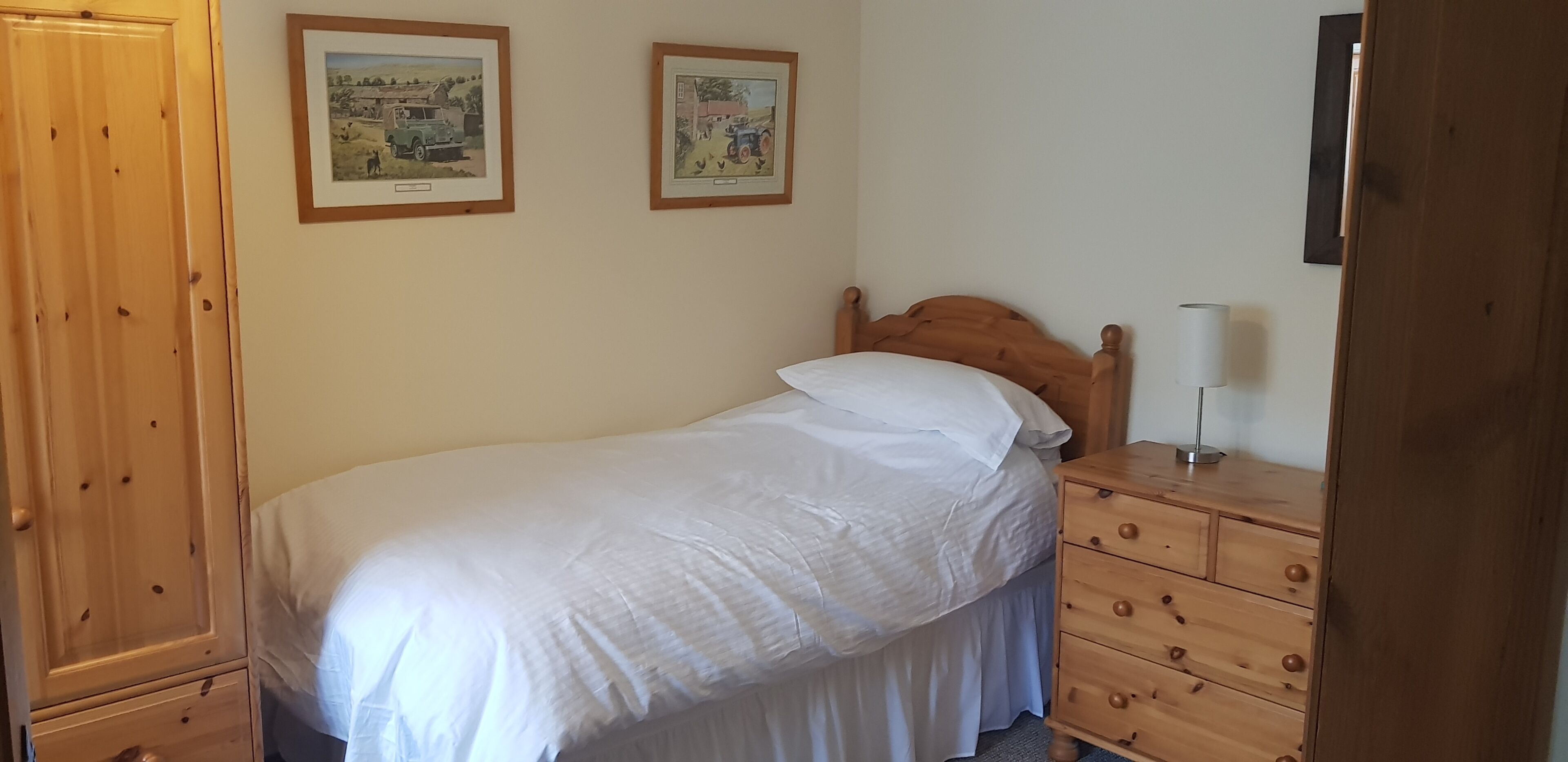A bedroom with a wooden bed, a wooden dresser, and two framed pictures on the wall.