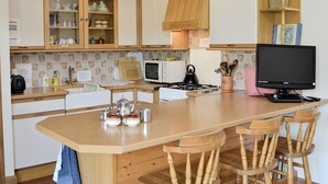 A kitchen with wooden cabinets, a central island with chairs, a stove, a microwave, and a television. - Cosy Cottage with Log burner very tranquil in gorgeous rural setting (Huntly)
