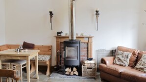 A cozy living room with a fireplace, a wooden bench, a leather sofa, and a dining table. - Cosy Cottage with Log burner very tranquil in gorgeous rural setting (Huntly)