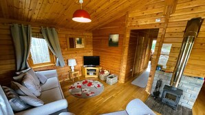 A cozy cabin interior with a sofa, a TV, a fireplace, and wooden walls. - Two bedroom logcabin with spectacular view and private balcony (Huntly)