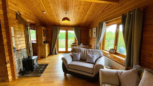 A cozy cabin interior with a wooden ceiling, a sofa, a dining table, and a fireplace. - Two bedroom logcabin with spectacular view and private balcony (Huntly)