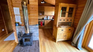 A cozy cabin interior with a wood-burning stove, wooden cabinets, and a kitchen area. - Two bedroom logcabin with spectacular view and private balcony (Huntly)