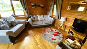 A cozy wooden cabin interior with a sofa, a television, and a round rug. - Two bedroom logcabin with spectacular view and private balcony (Huntly)
