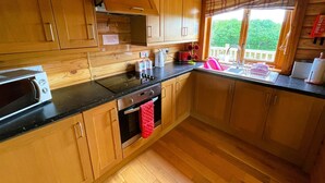 A kitchen with wooden cabinets, a stove, a sink, and a window with a view of greenery. - Two bedroom logcabin with spectacular view and private balcony (Huntly)